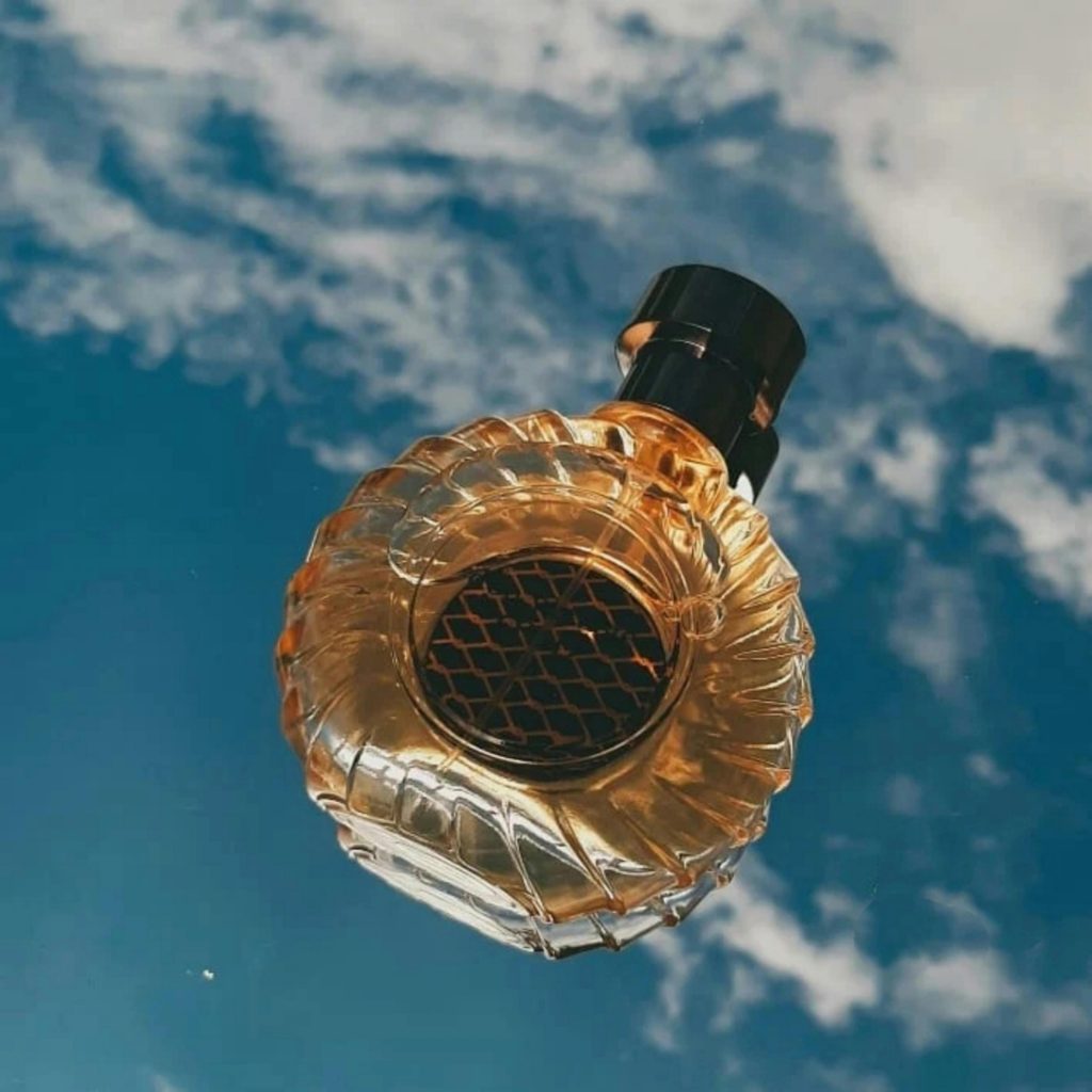 Elegant glass perfume bottle with blue sky and clouds backdrop.
