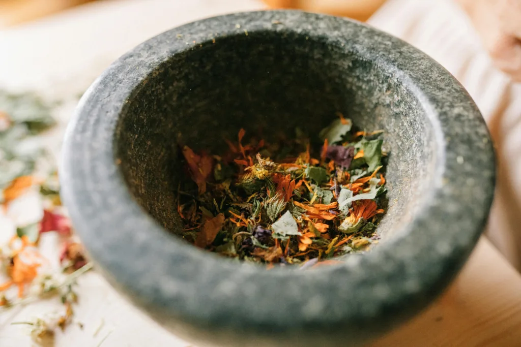 A granite mortar filled with colorful dried herbs and petals on a wooden surface.
