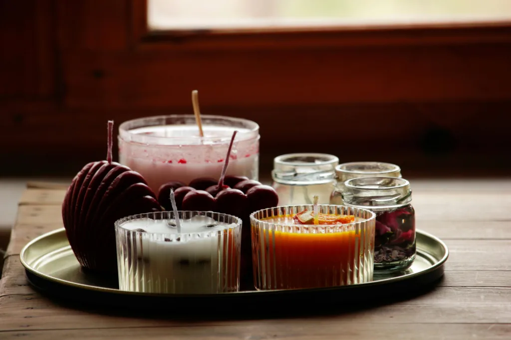 A variety of scented candles in glass jars on a tray by a window, creating a warm ambiance.